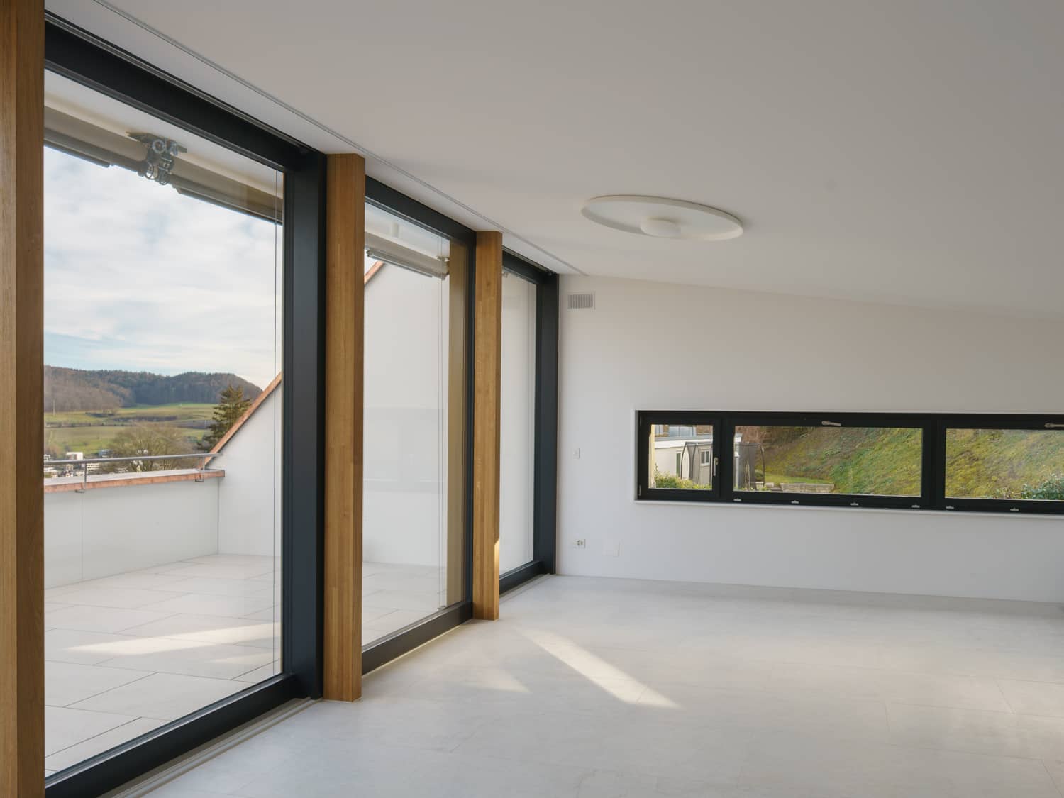 Von einem leeren Wohnraum f&uuml;hren drei bodenlange Fenster auf eine Terrasse
